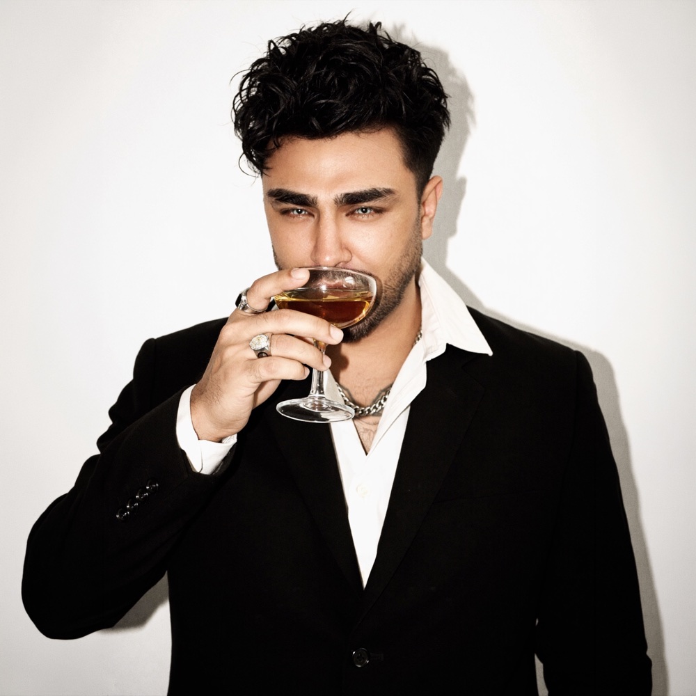 Arian Romal wearing a black suit and holding a glass