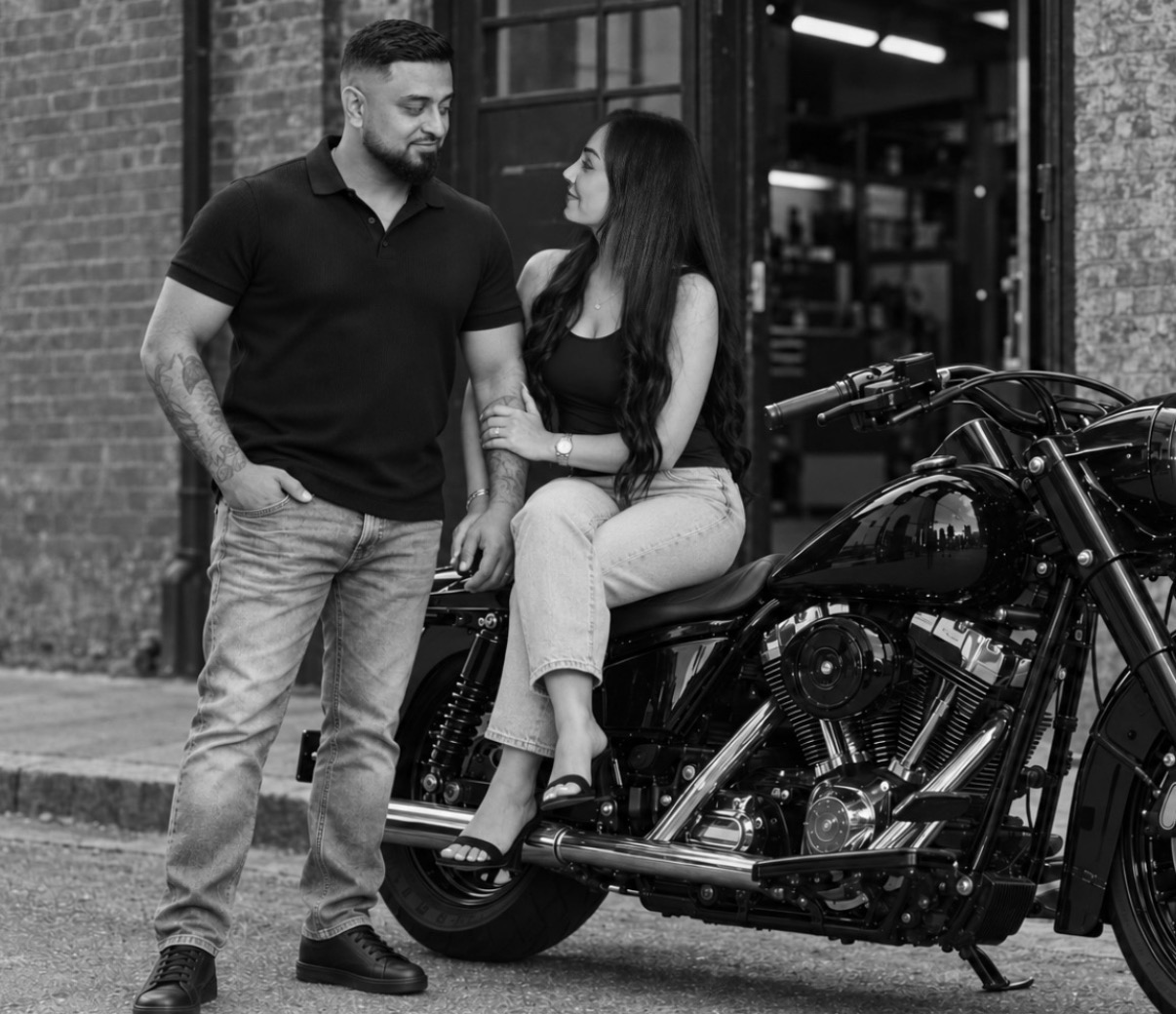 Omid with his wife and a black Harley-Davidson outside a brick workshop